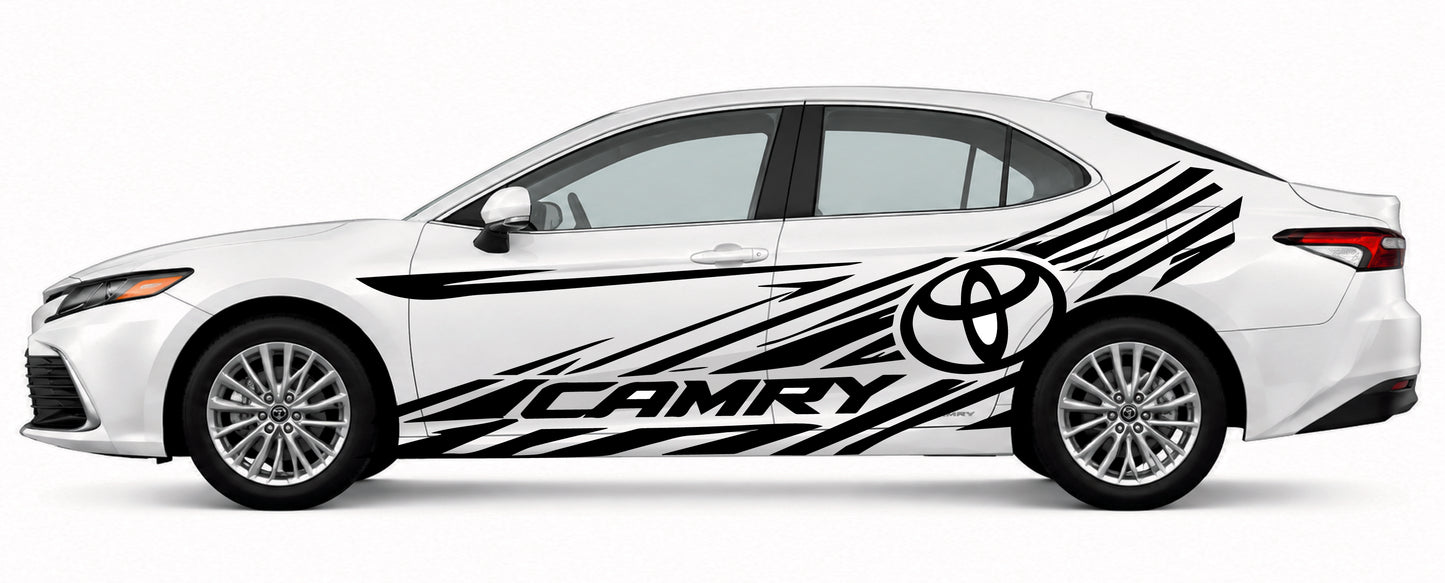 A white Toyota Camry sedan shown in side profile on a light gray studio background, decorated with large black graphic decals including the Toyota emblem and the word CAMRY.