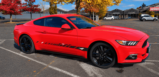 Red Mustang car parked in a lot with trees and buildings in the background